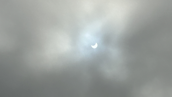 Partially eclipsed Sun peeking through clouds